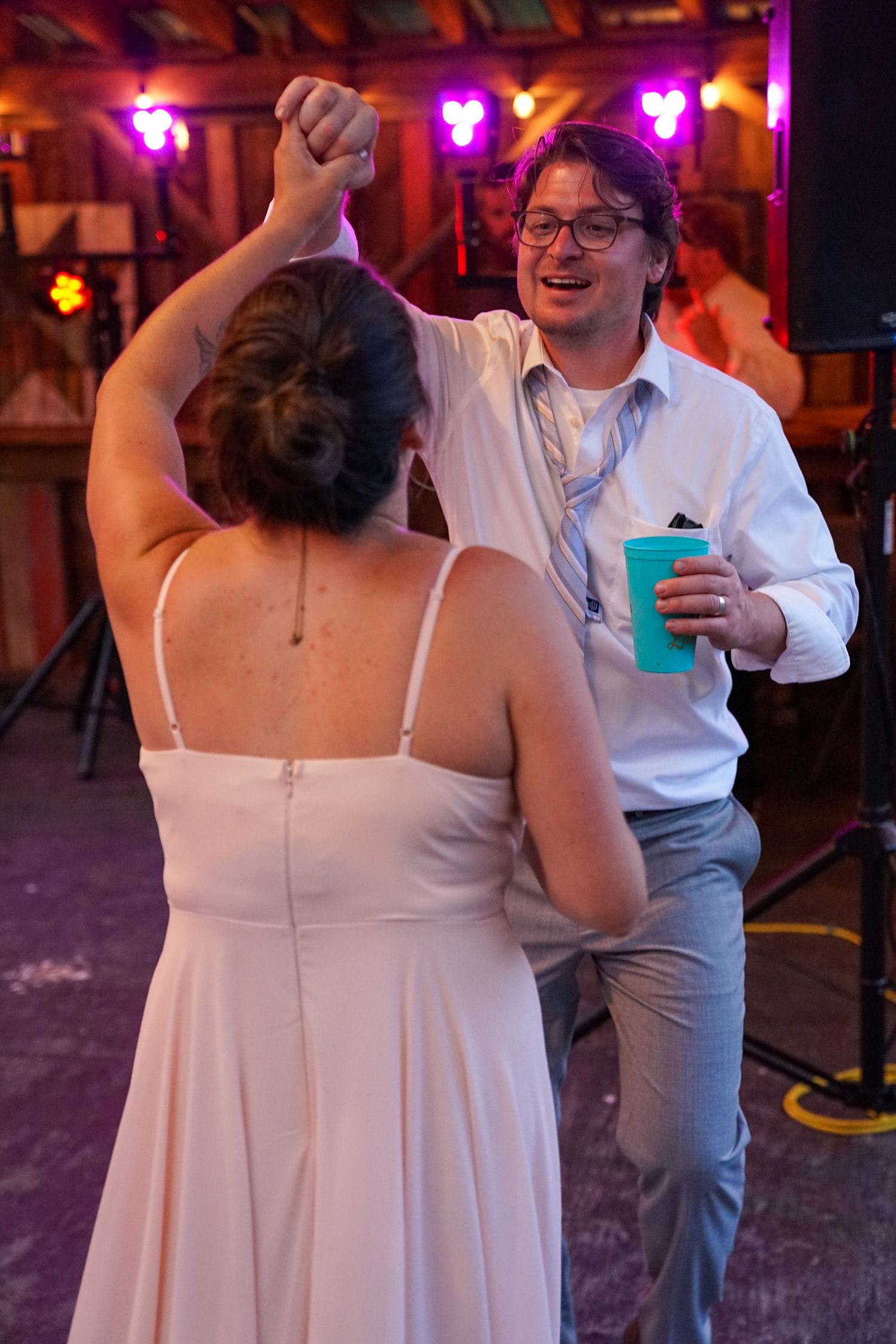 A couple dancing together at a reception with purple lighting and the person in white holding a blue drink.