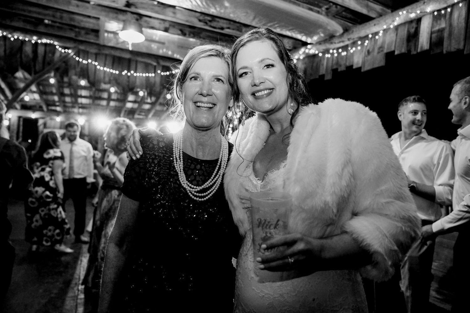 Two guests at a celebration pose together under festive lights in a black and white photo.