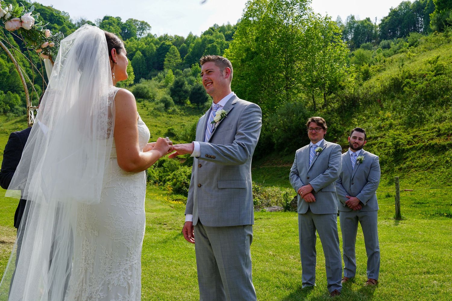 Wedding party stands on a lush green hillside during an outdoor summer ceremony.