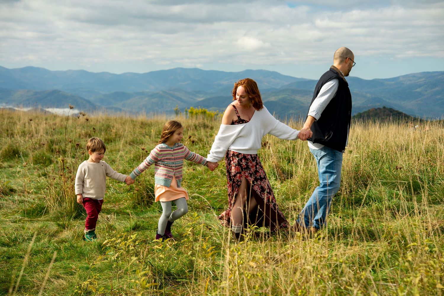 A group of people walking together through a scenic mountain meadow with rolling hills in the background.