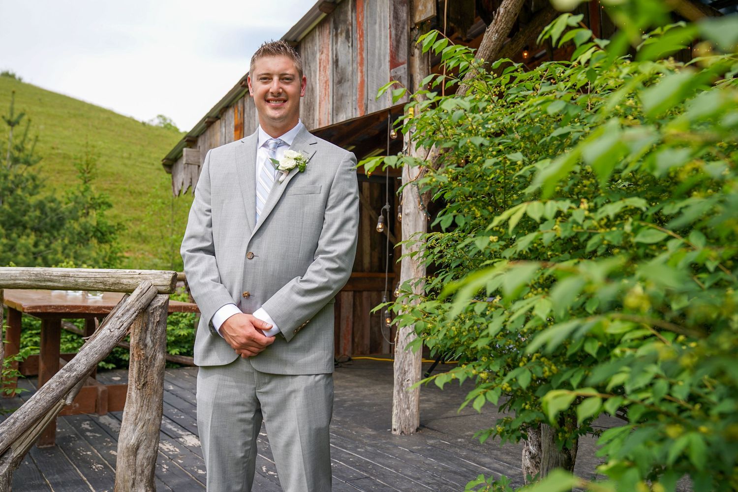 A couple poses for wedding photos in a lush green meadow setting with mountains in the background.