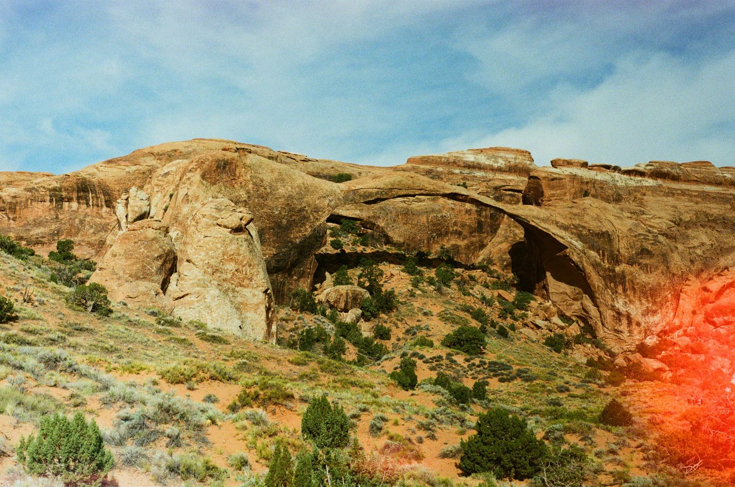 Landscape photo of Landscape Arch, a natural sandstone bridge formation in Arches National Park against blue sky. 35mm film