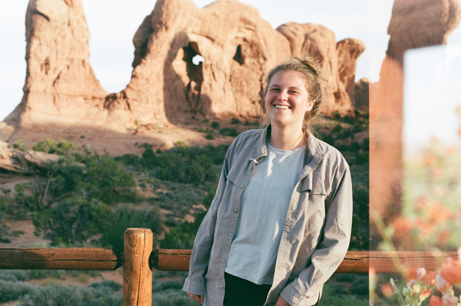 Person relaxing along wooden fence at scenic desert overlook with red rock formations.