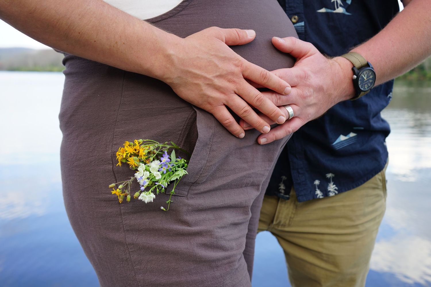 Close-up of hands holding a small bouquet of yellow and white wildflowers against brown fabric.