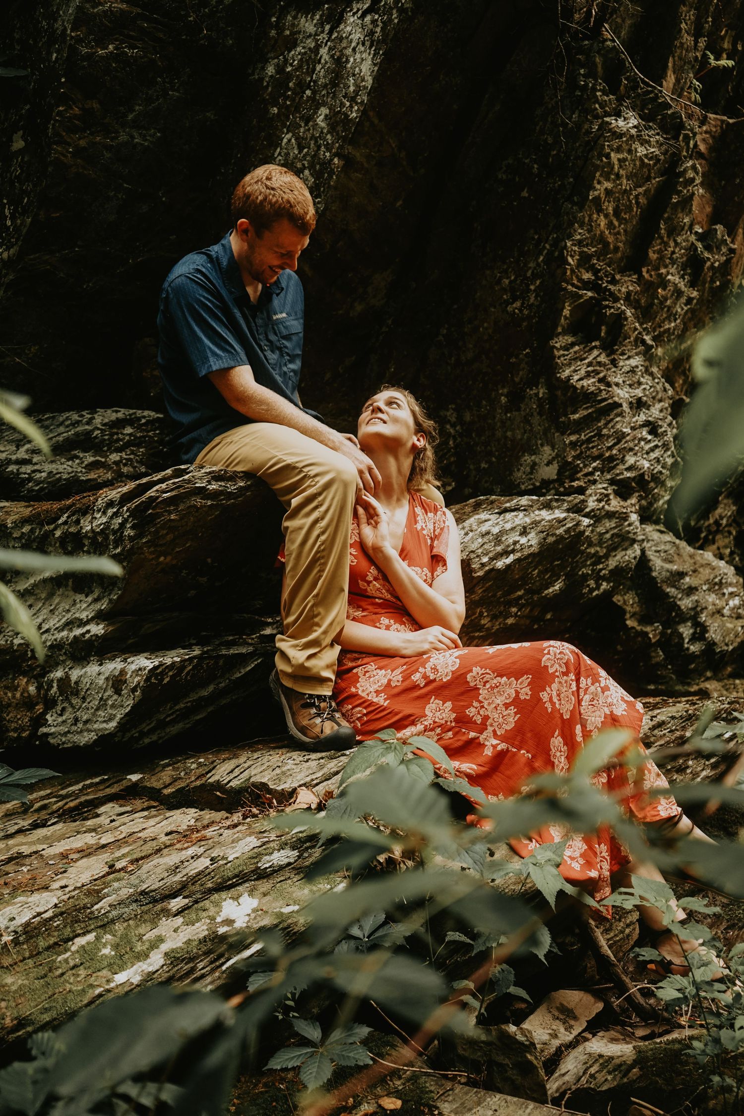 A romantic couple poses on rocky terrain in a forest setting.