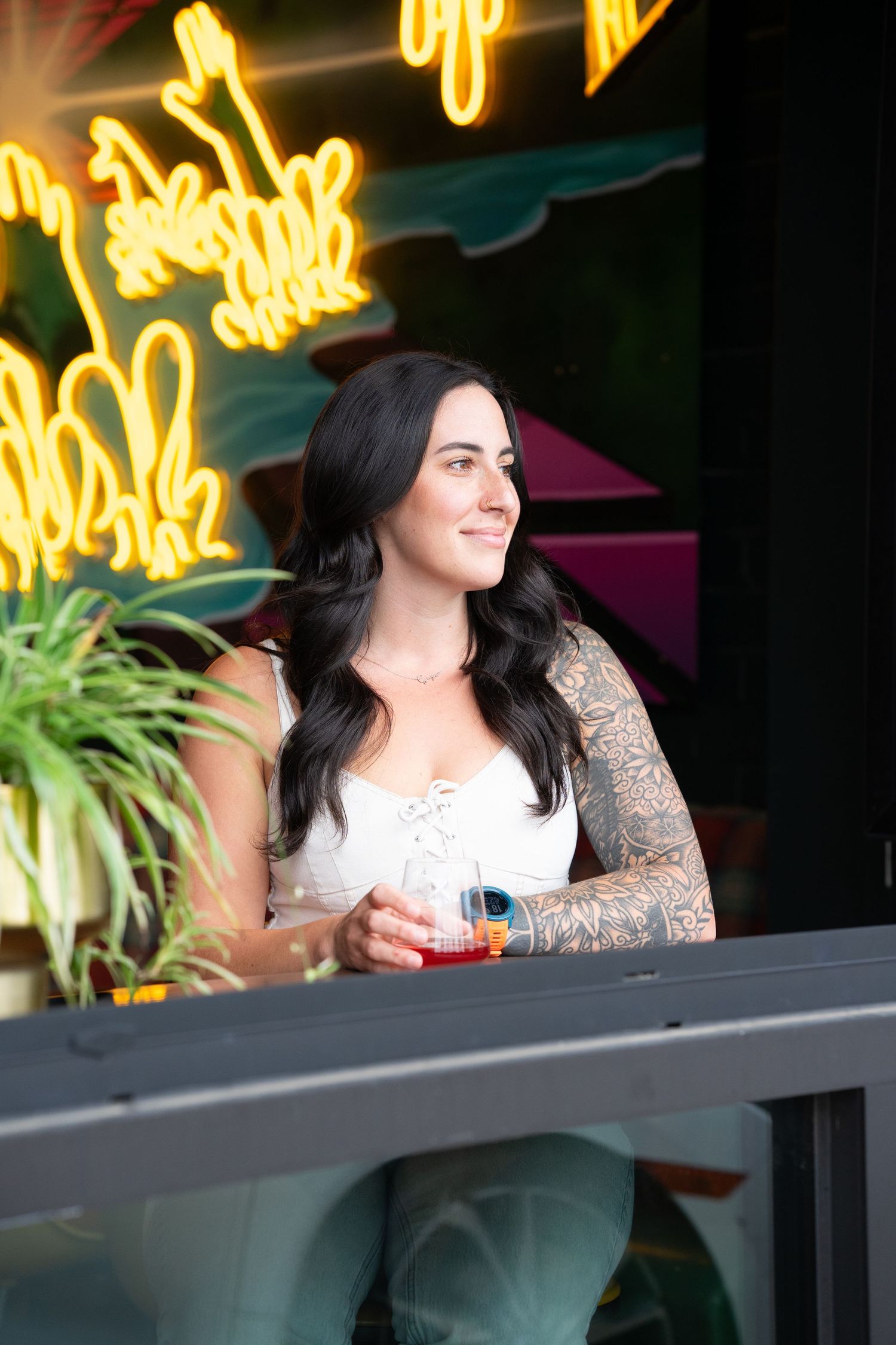 A woman with dark hair wearing white looks out from a balcony with neon signage glowing in the background.