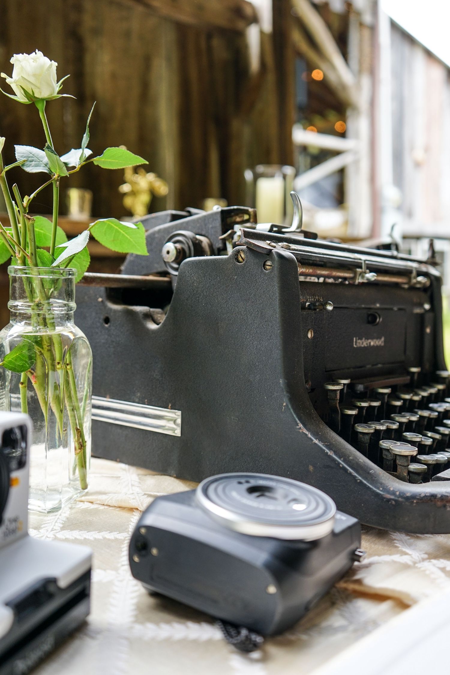Vintage black typewriter sits on white surface with white roses in glass vase creating romantic writing atmosphere.