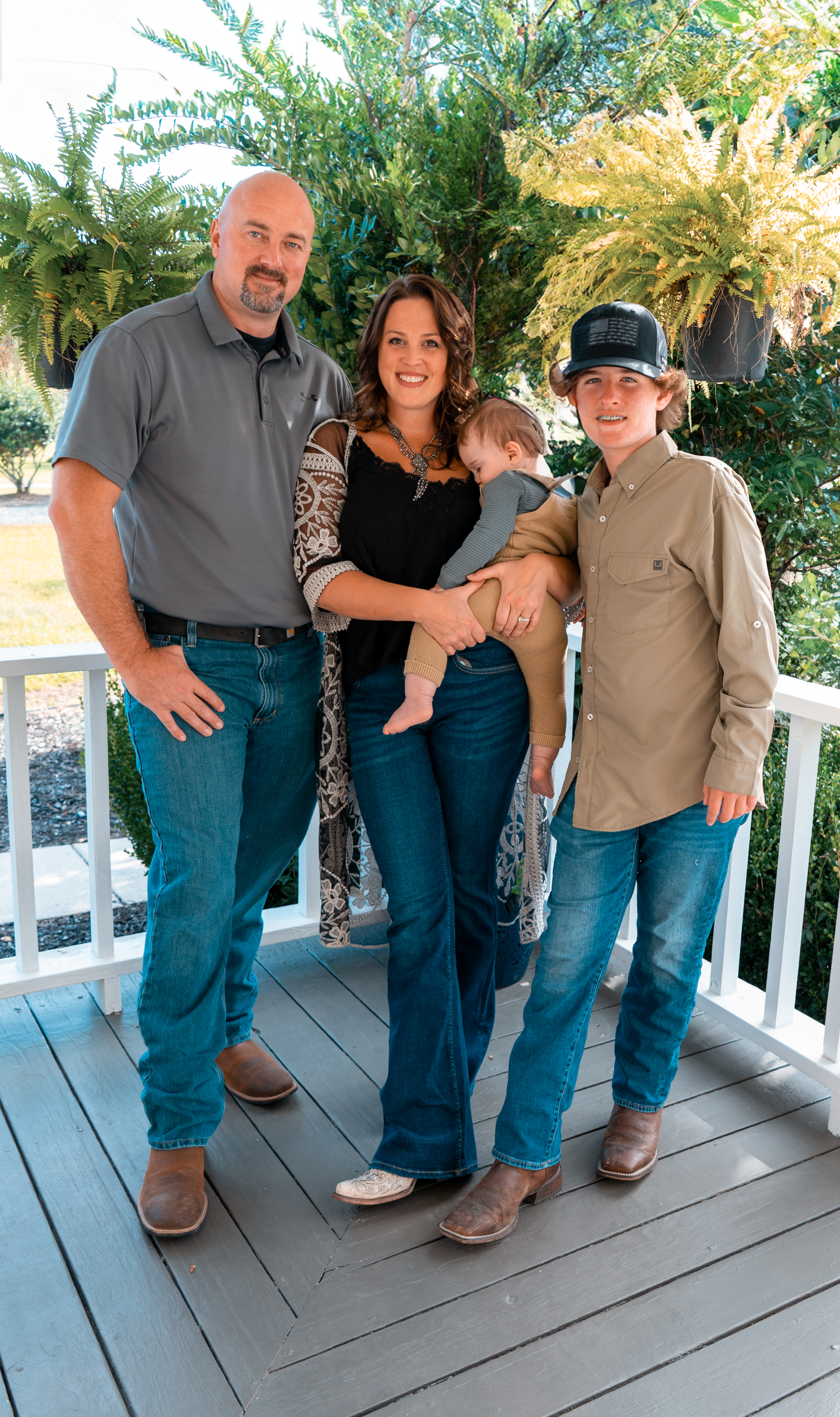 Family portrait on a wooden deck with tropical plants and greenery in the background.