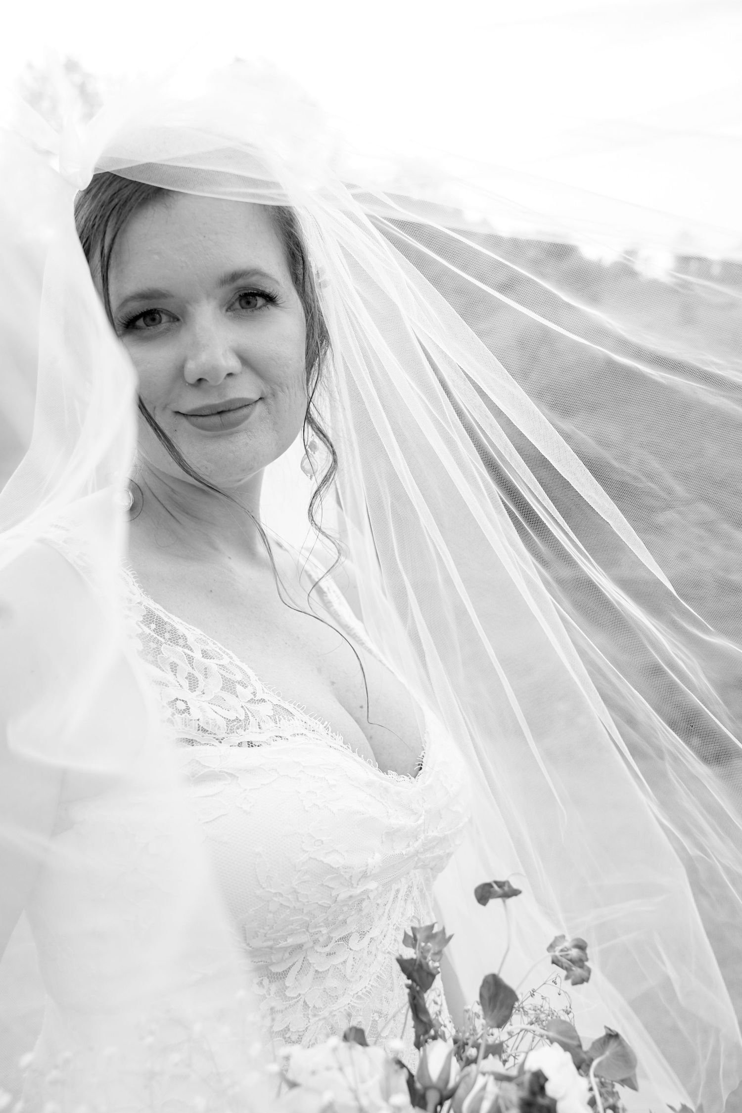 A bride in a white lace wedding dress holds a bouquet while her veil flows in the breeze.