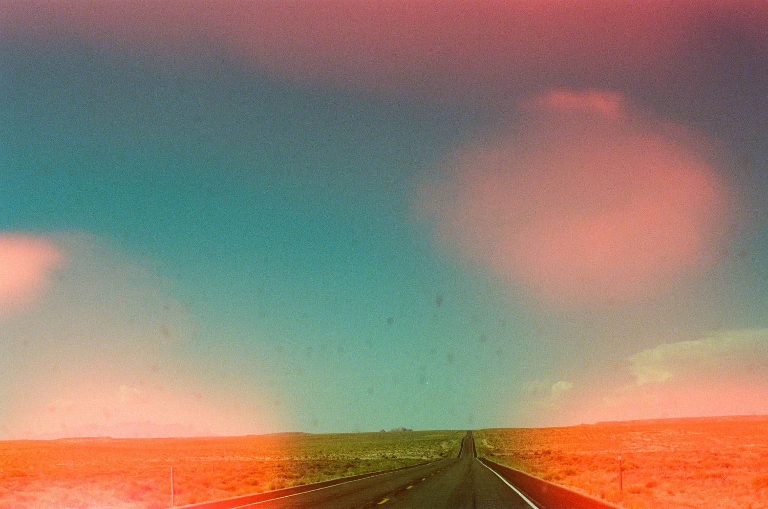 Scenic desert road stretching to horizon under dramatic pink and turquoise sunset sky.