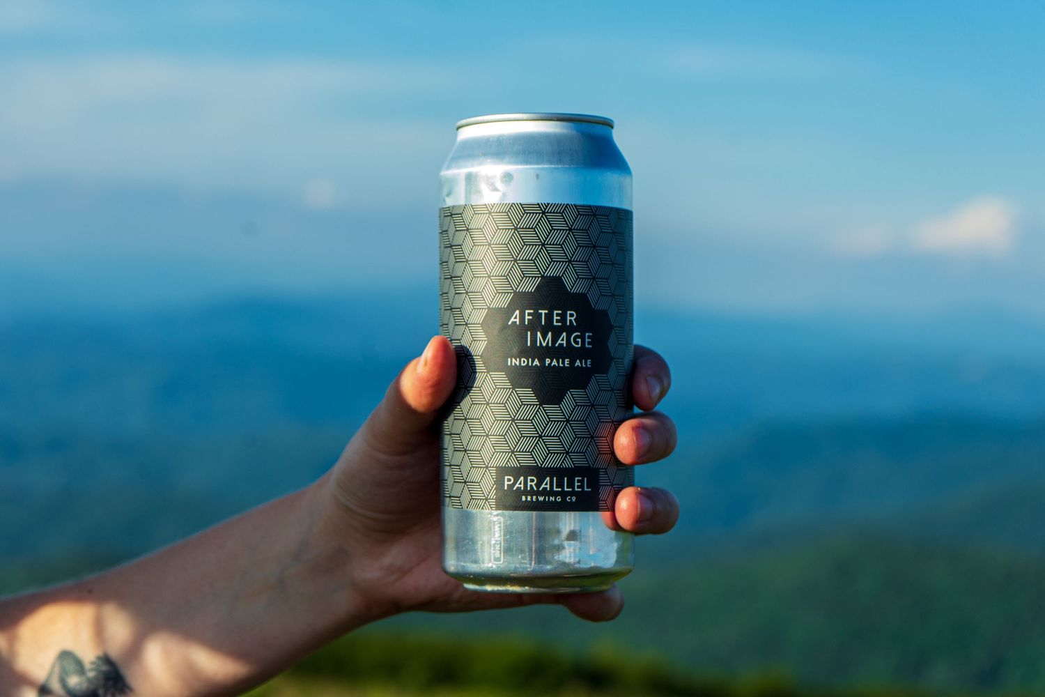 Beer cans held up against a blue mountain vista backdrop.