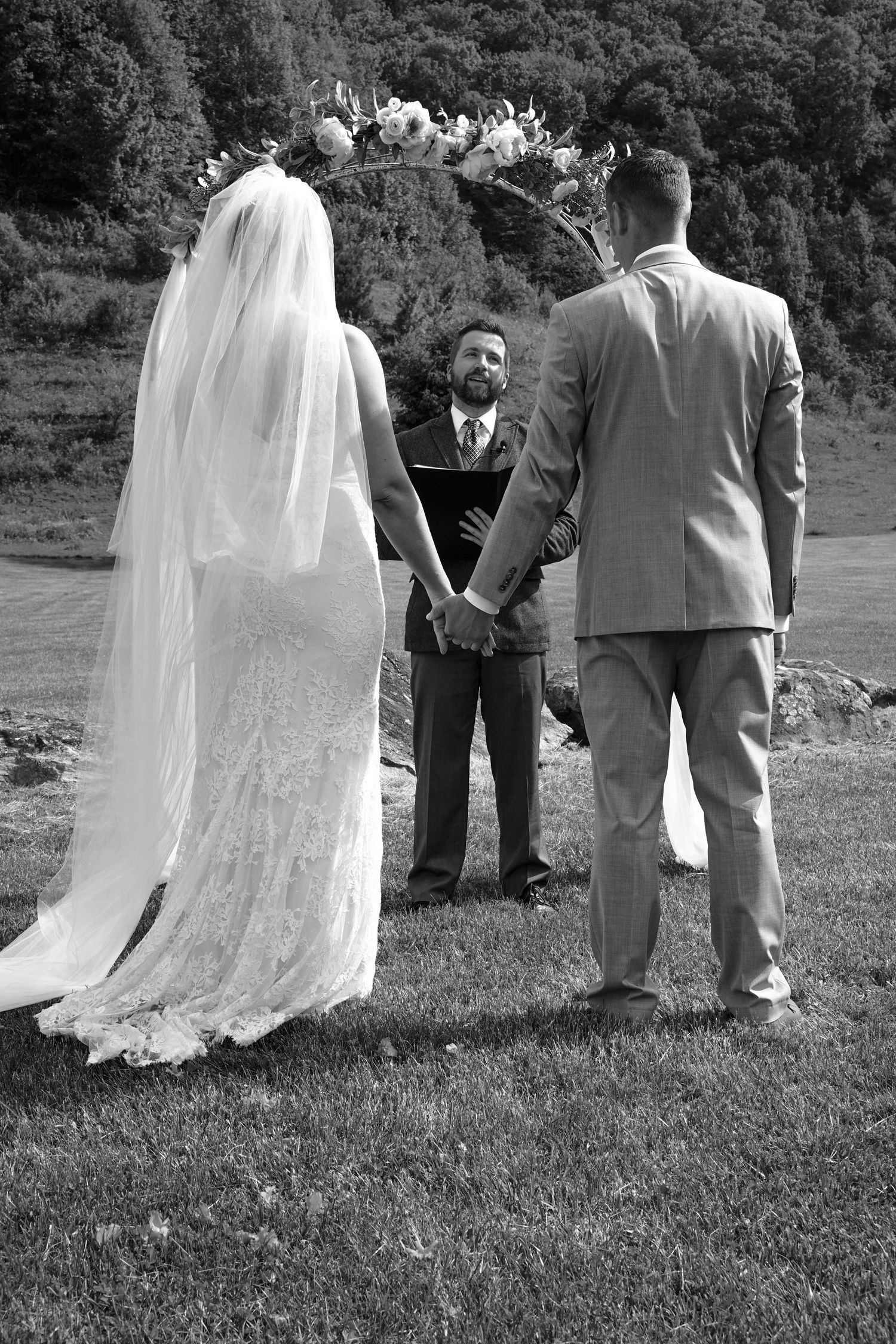 A series of black and white wedding photos showing a couple and guests standing on grass in formal attire.