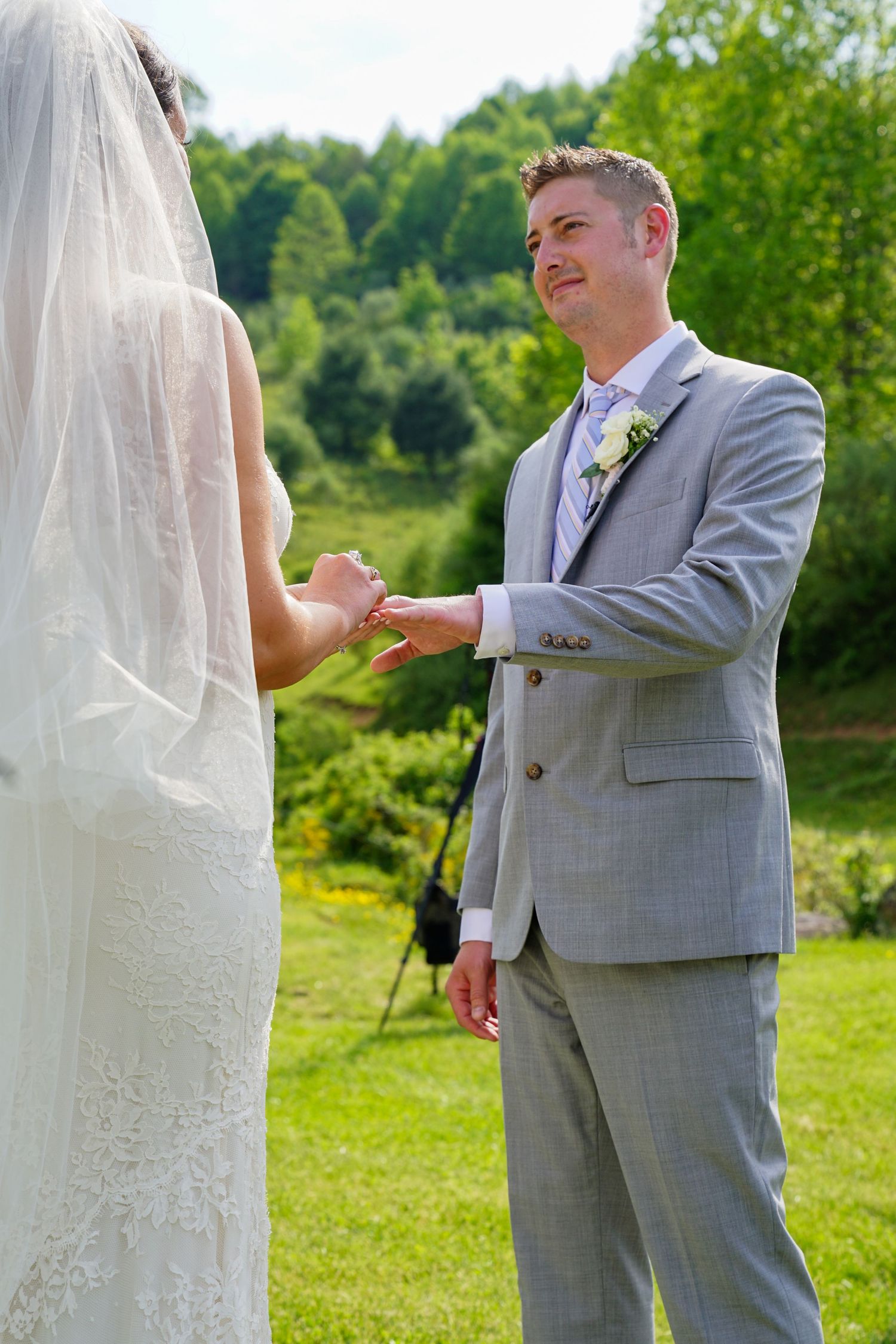 A wedding couple shares a tender moment outdoors in a grassy field with trees in the background.