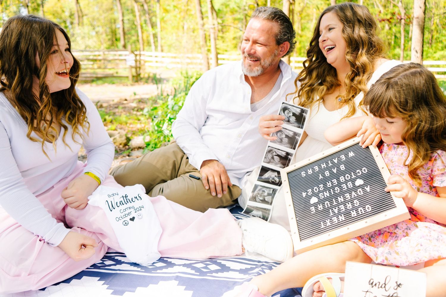 A family gathering on a picnic blanket with a letter board displaying a special message.