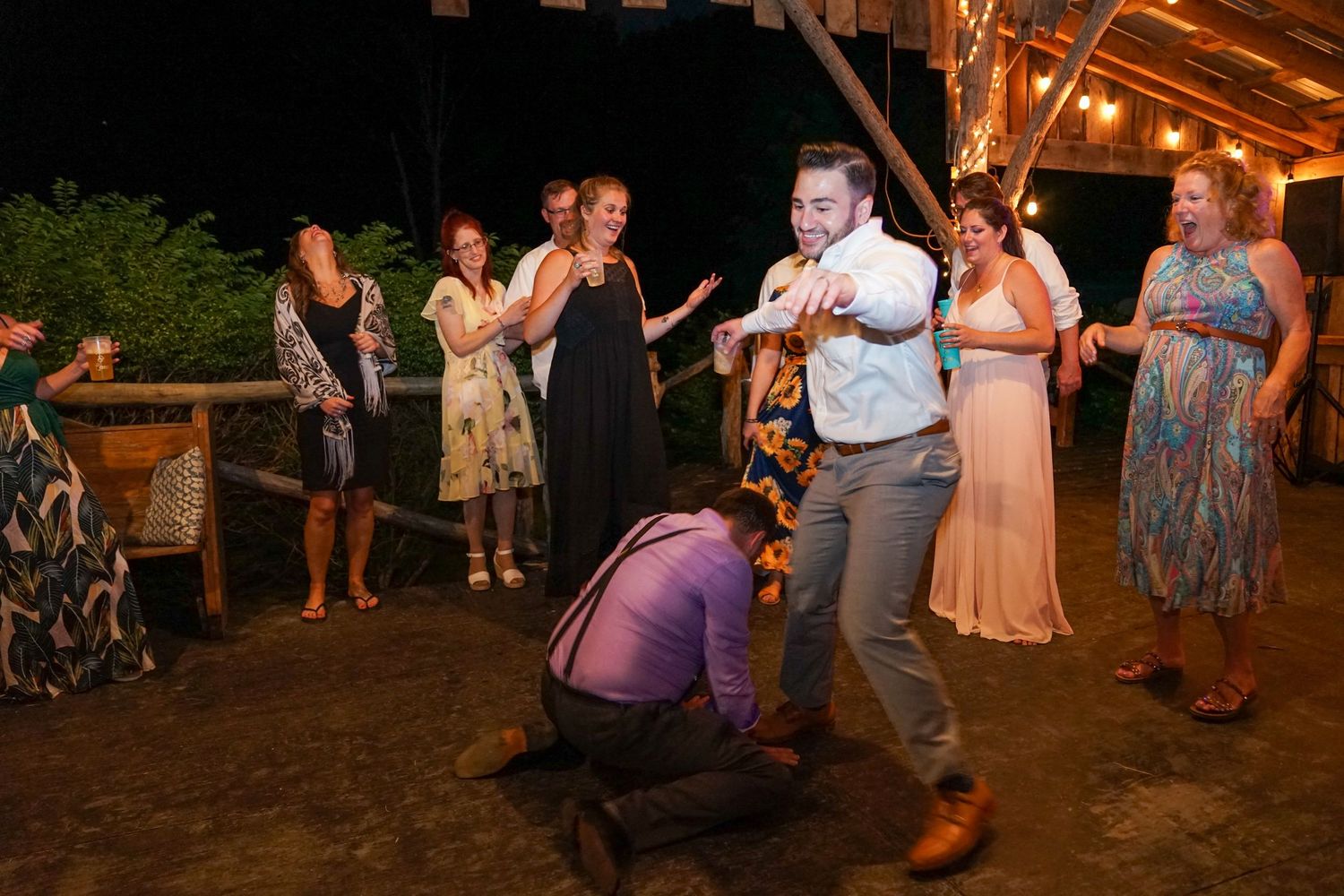 People dancing and celebrating at an outdoor evening wedding reception under string lights.