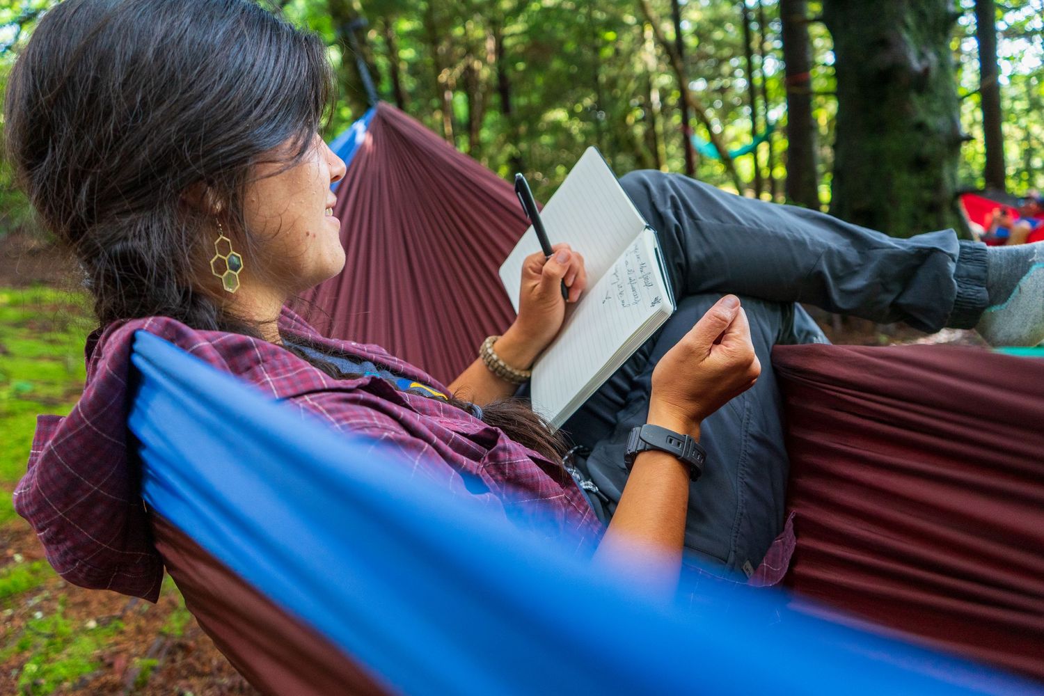 Relaxing in a purple hammock while reading a book in a peaceful forest setting.
