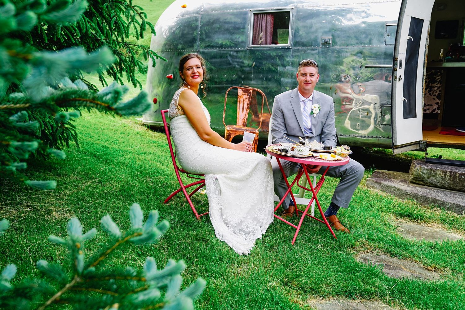 Couple enjoys an intimate outdoor garden party with vintage furniture and table settings in a lush green setting.