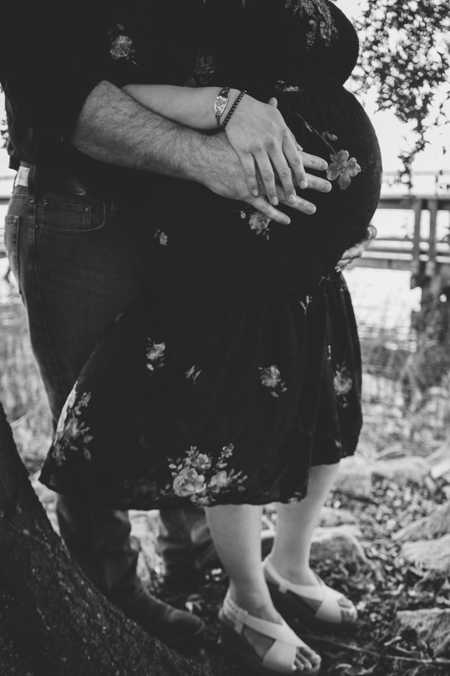 An intimate black and white portrait showing hands embracing on a wooden deck.