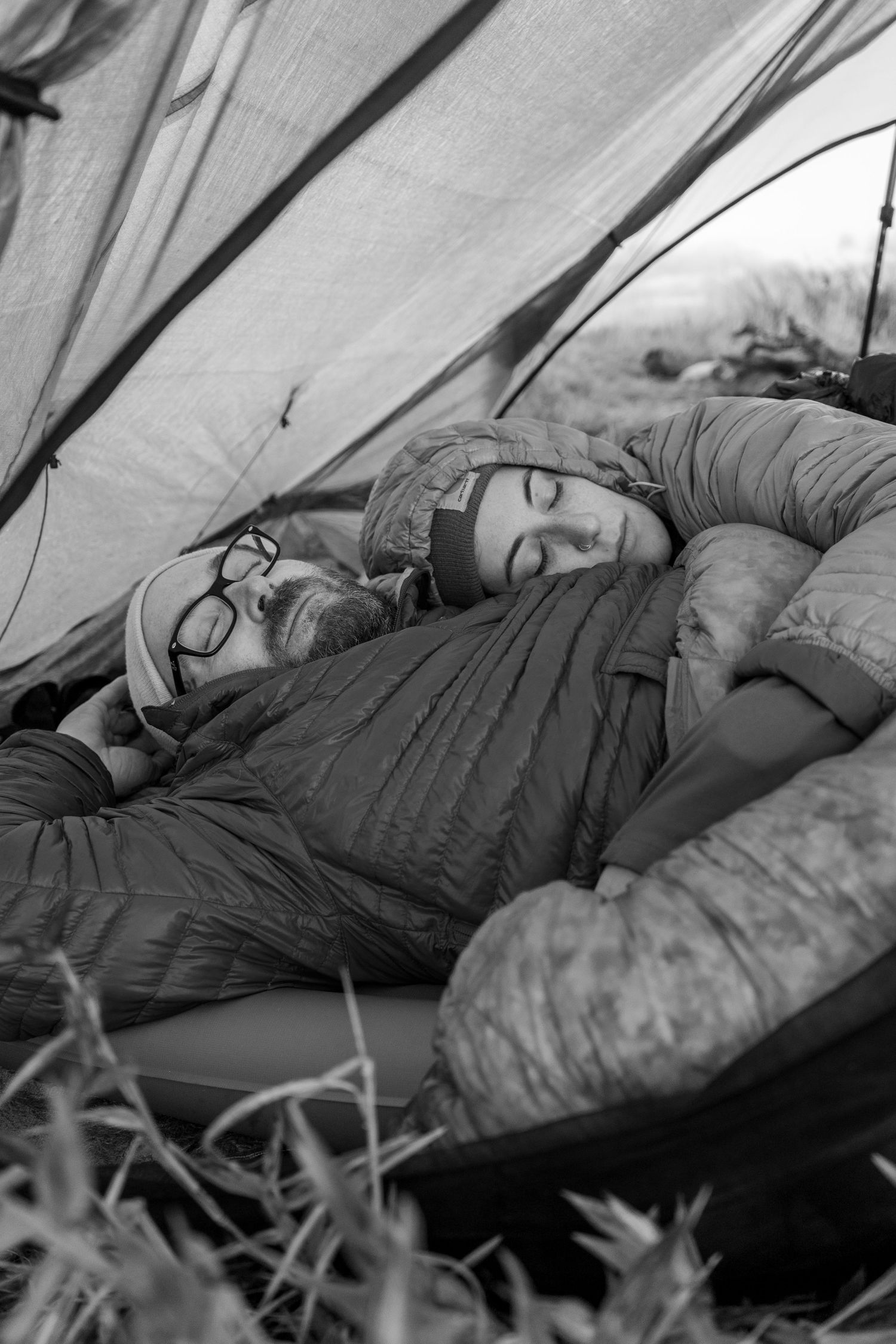 Black and white photo of campers resting in sleeping bags inside a tent.