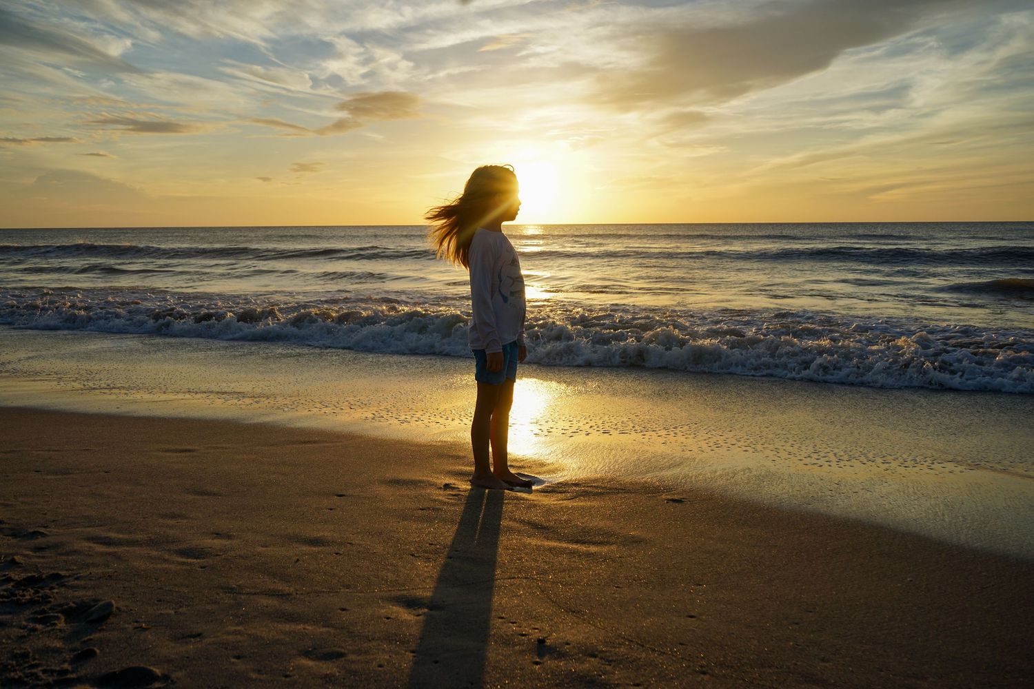 Silhouette against golden sunset sky on empty beach.
