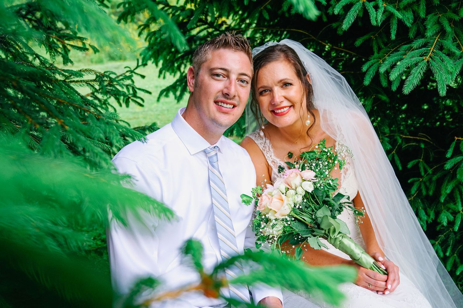 A wedding couple shares joyful moments together in a lush green garden setting during their outdoor photo session.