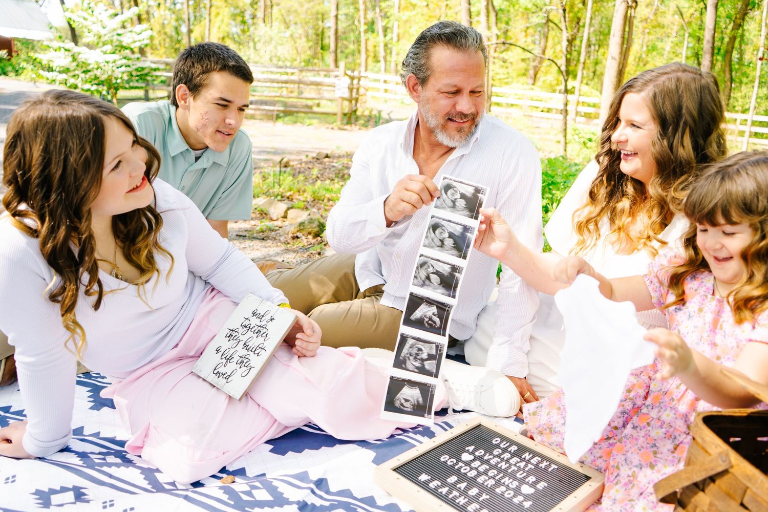 Group sitting outdoors looking at ultrasound photos together with excited expressions.