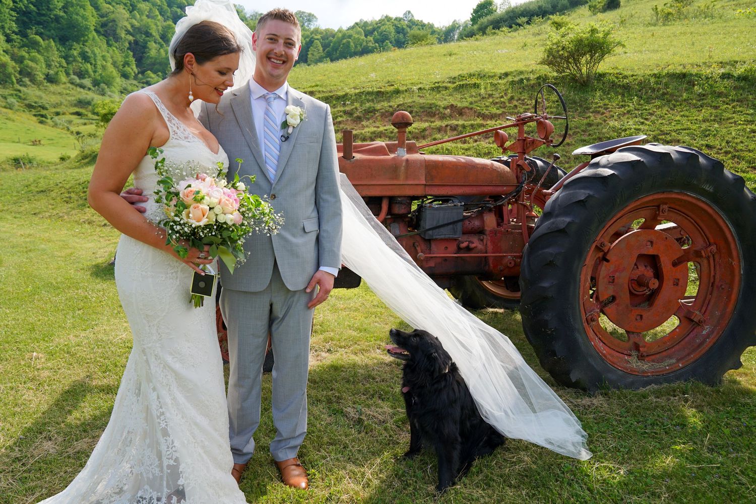 Newlyweds pose for photos in a rustic field with vintage red tractors on their wedding day.