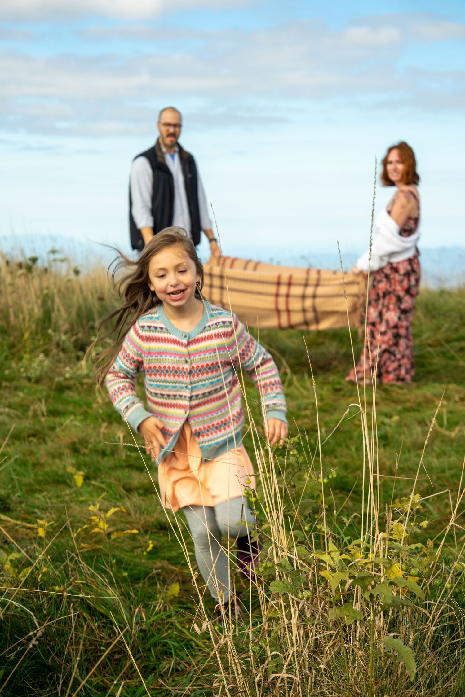 A joyful family explores a grassy meadow with wildflowers on a sunny day.