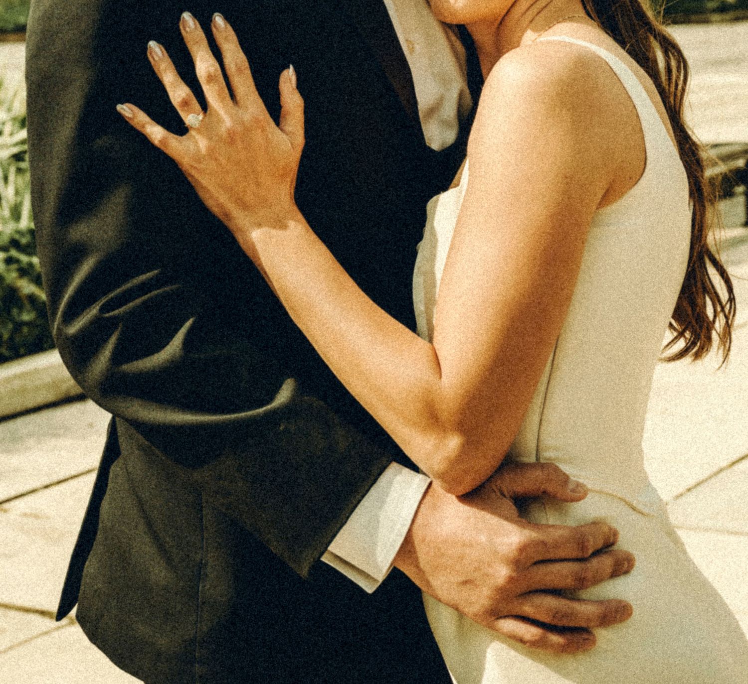 Close-up of bride and groom embracing, showing wedding rings and elegant formal attire.