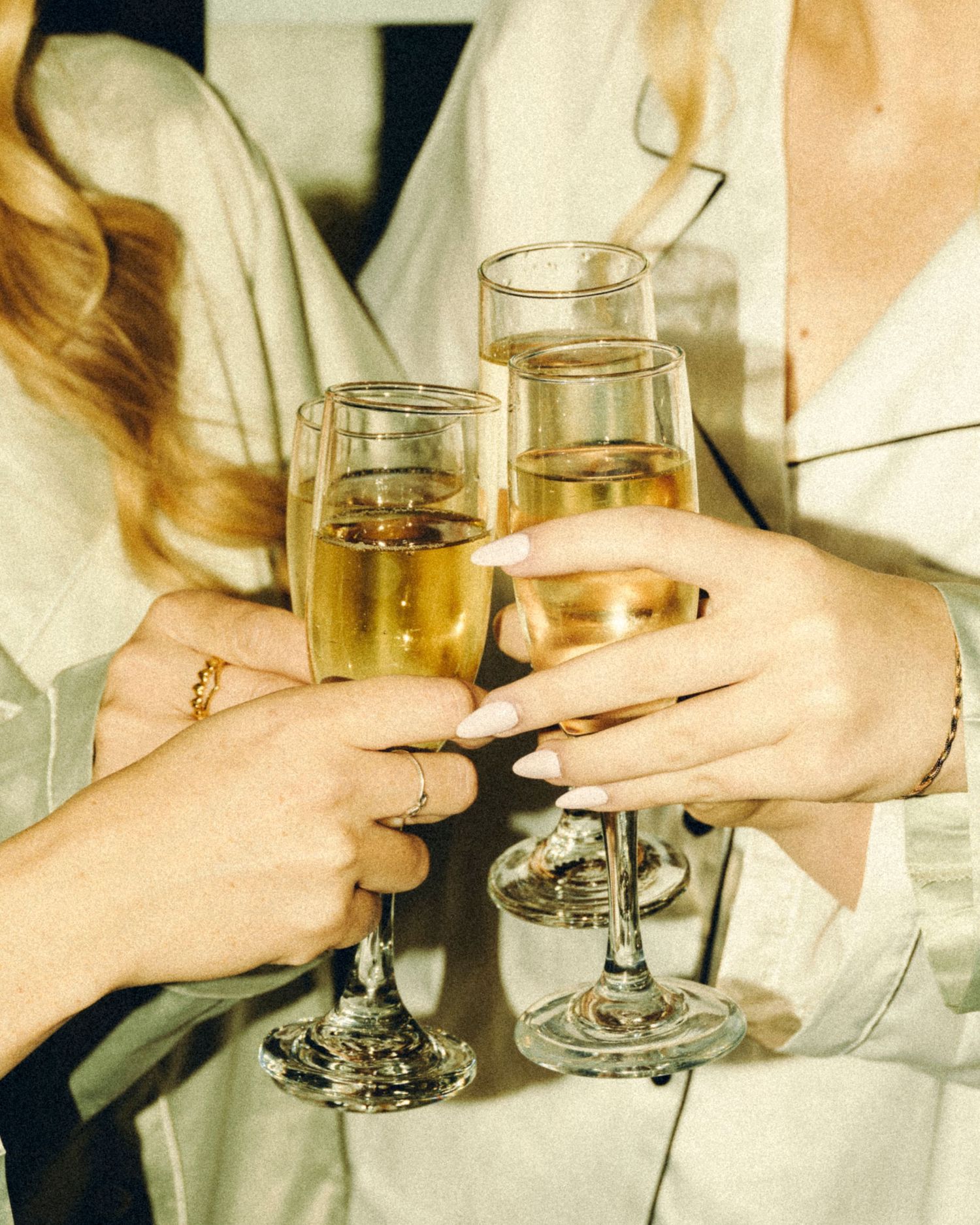Three women in white robes toasting with champagne flutes in a celebratory wedding morning cheers.