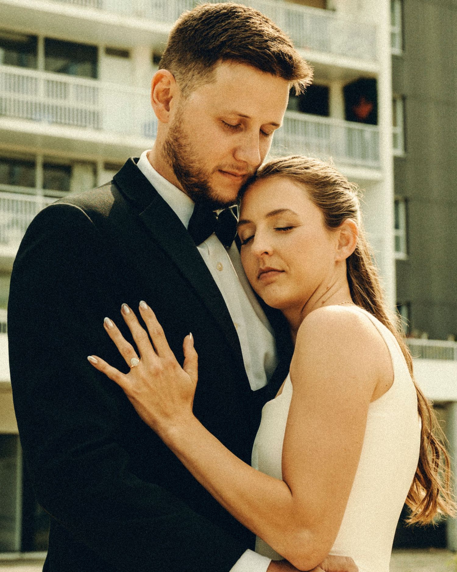 Bride resting her head on groom's chest in a tender embrace during wedding portrait.