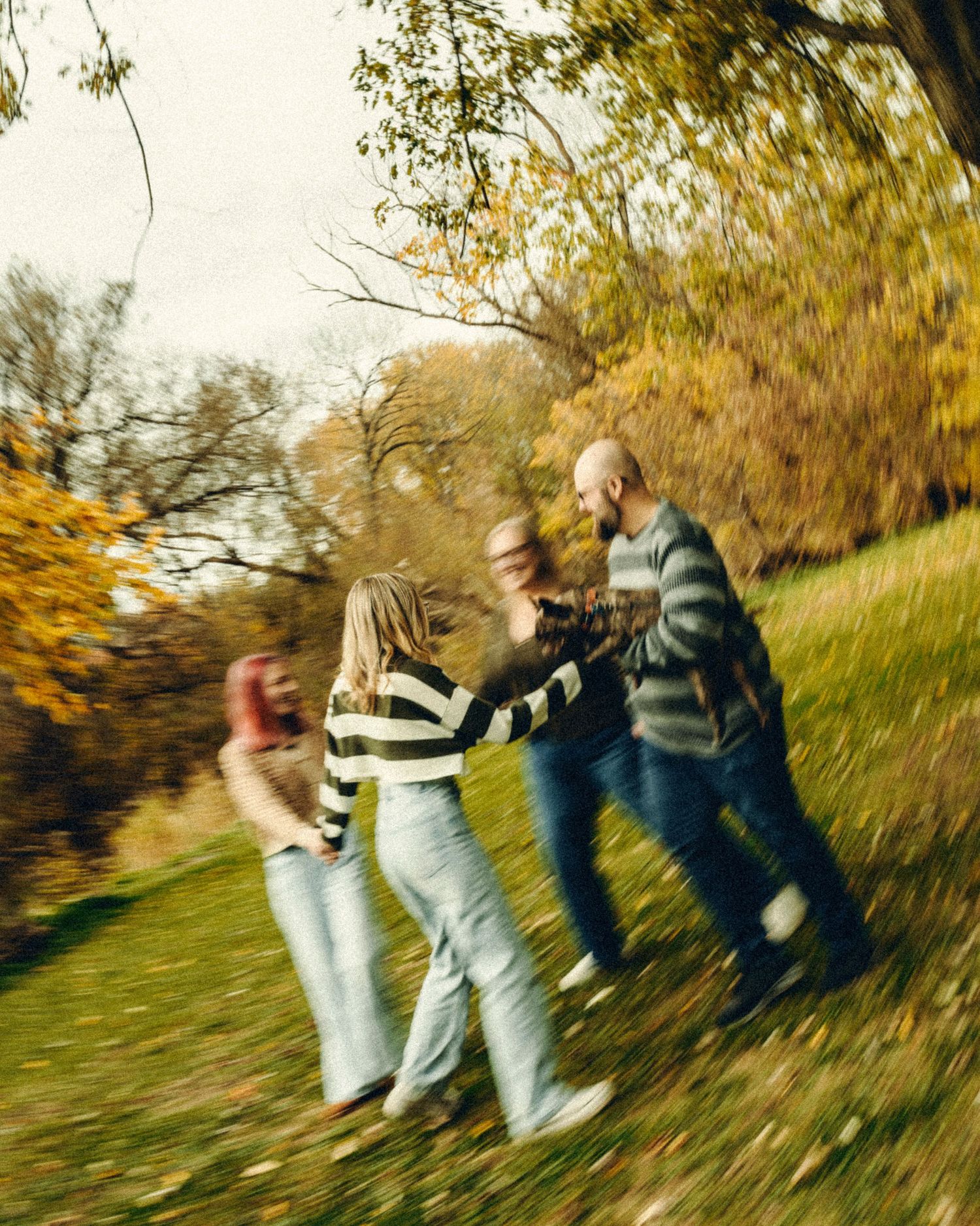 Family holding hands spinning together in colorful autumn park with golden fall foliage.