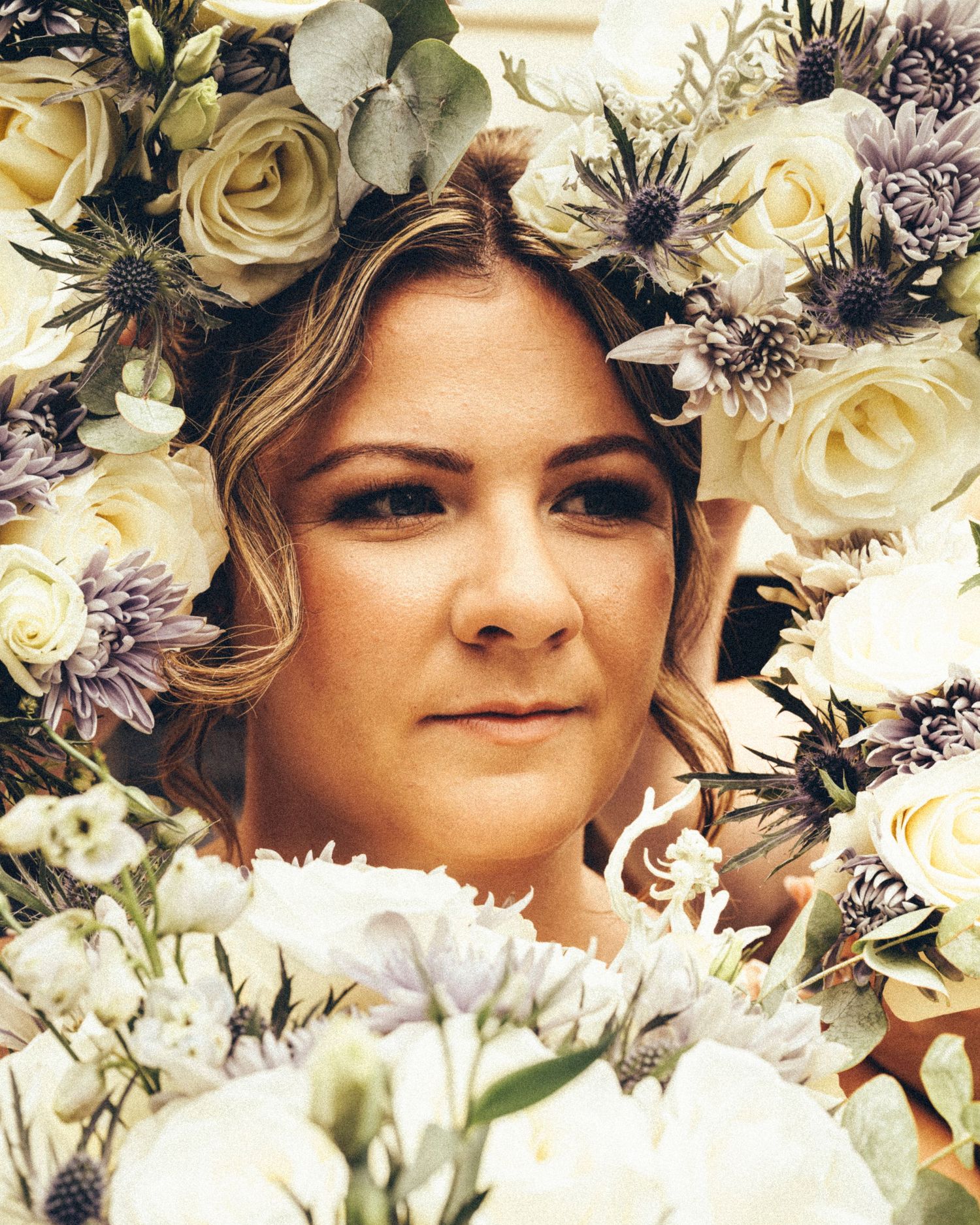 Bride surrounded by white roses and lavender flowers with a floral crown at her wedding.