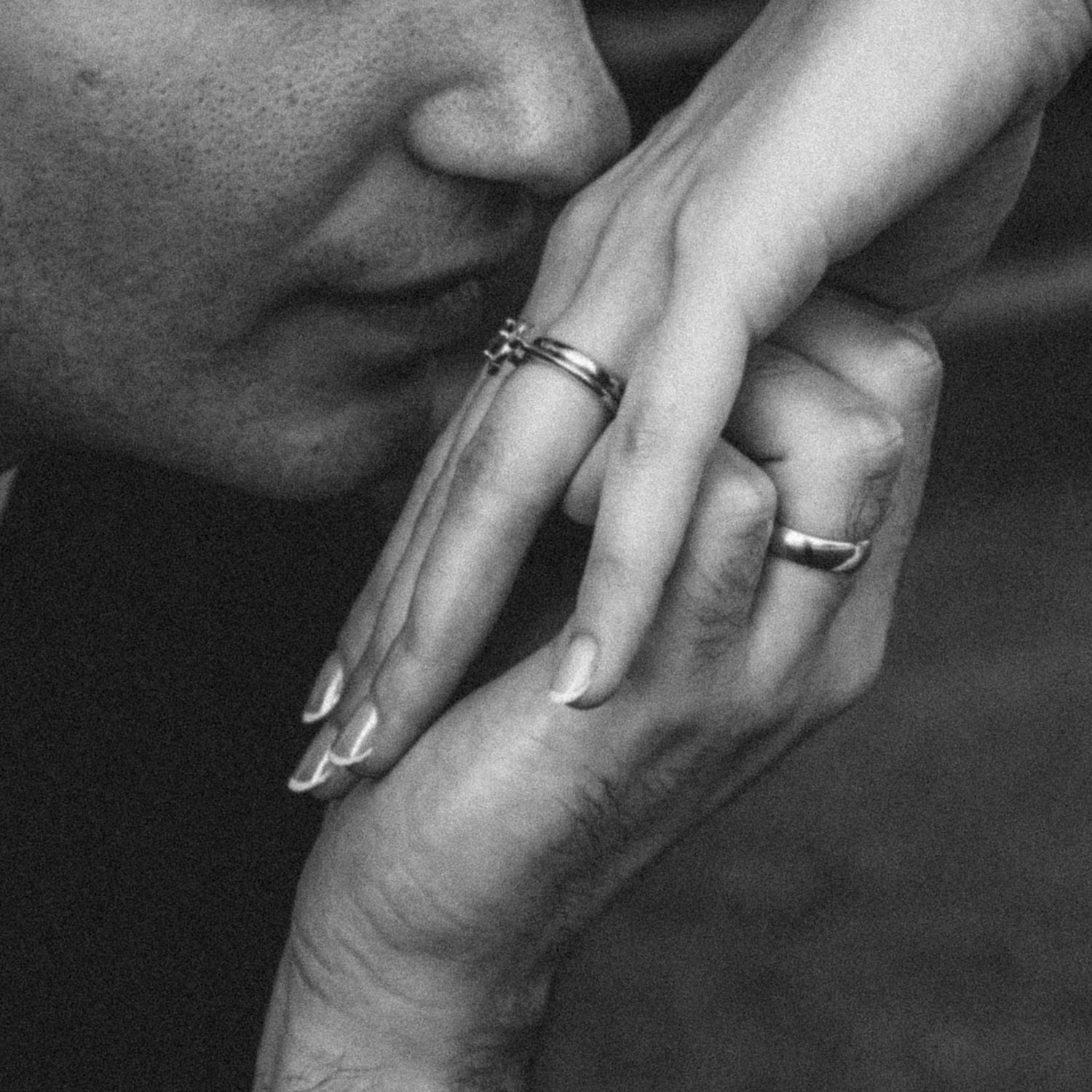 Groom kissing bride's hand adorned with wedding rings in black and white.