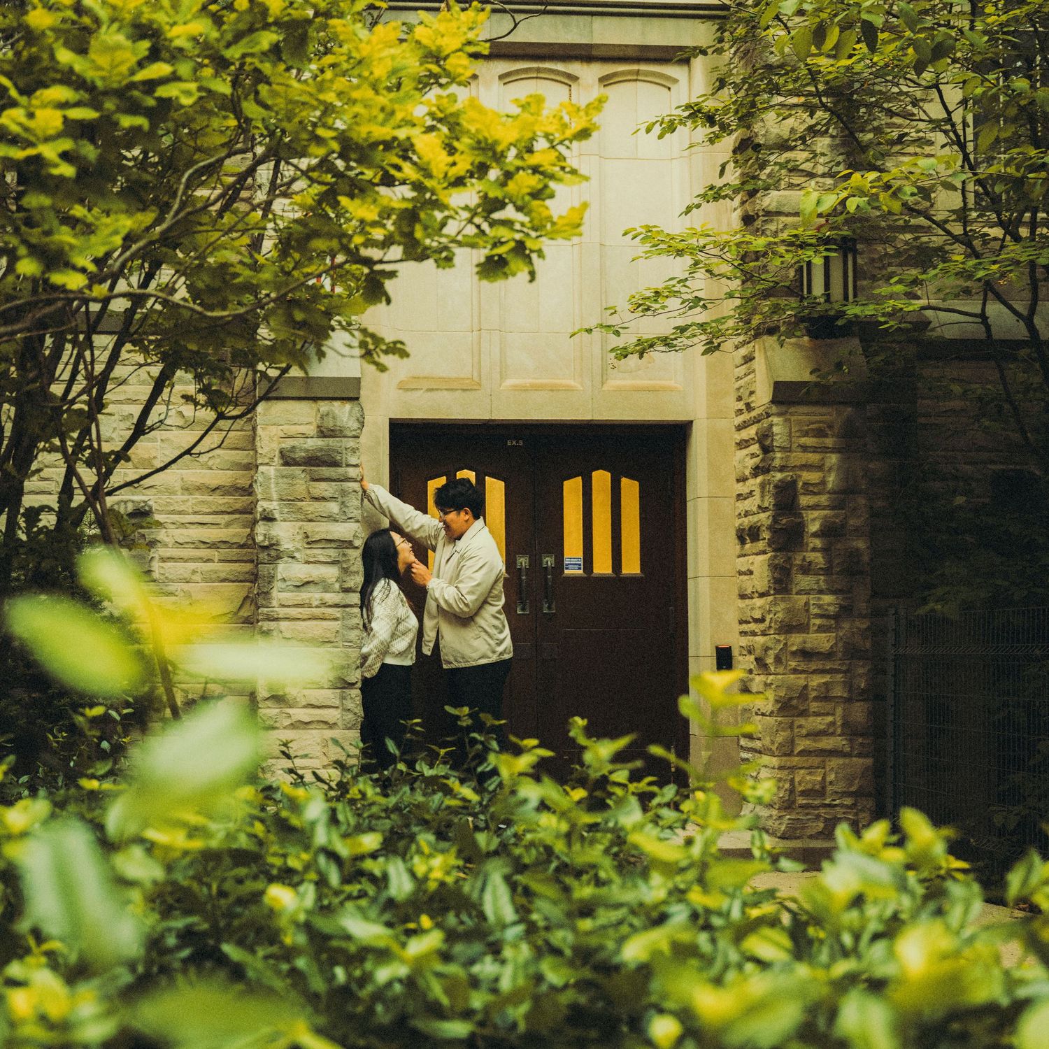 Romantic couple embracing in a doorway framed by green foliage at a stone building entrance.