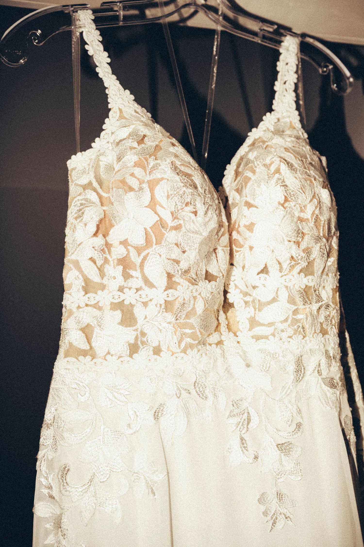 Elegant lace wedding dress with floral embroidery and spaghetti straps hanging on clear hanger.