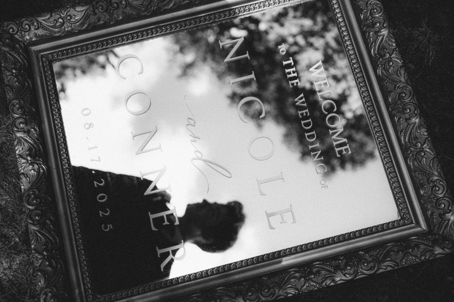 Black and white photo of a framed wedding welcome sign for Nicole and Connor dated 08.17.2025.