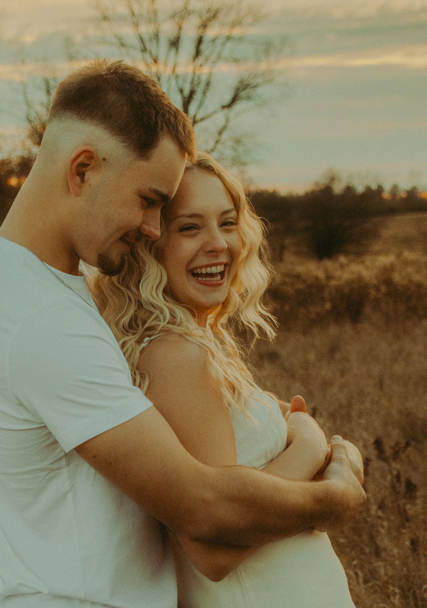 Couple embracing and laughing together in golden sunset light in an autumn field.