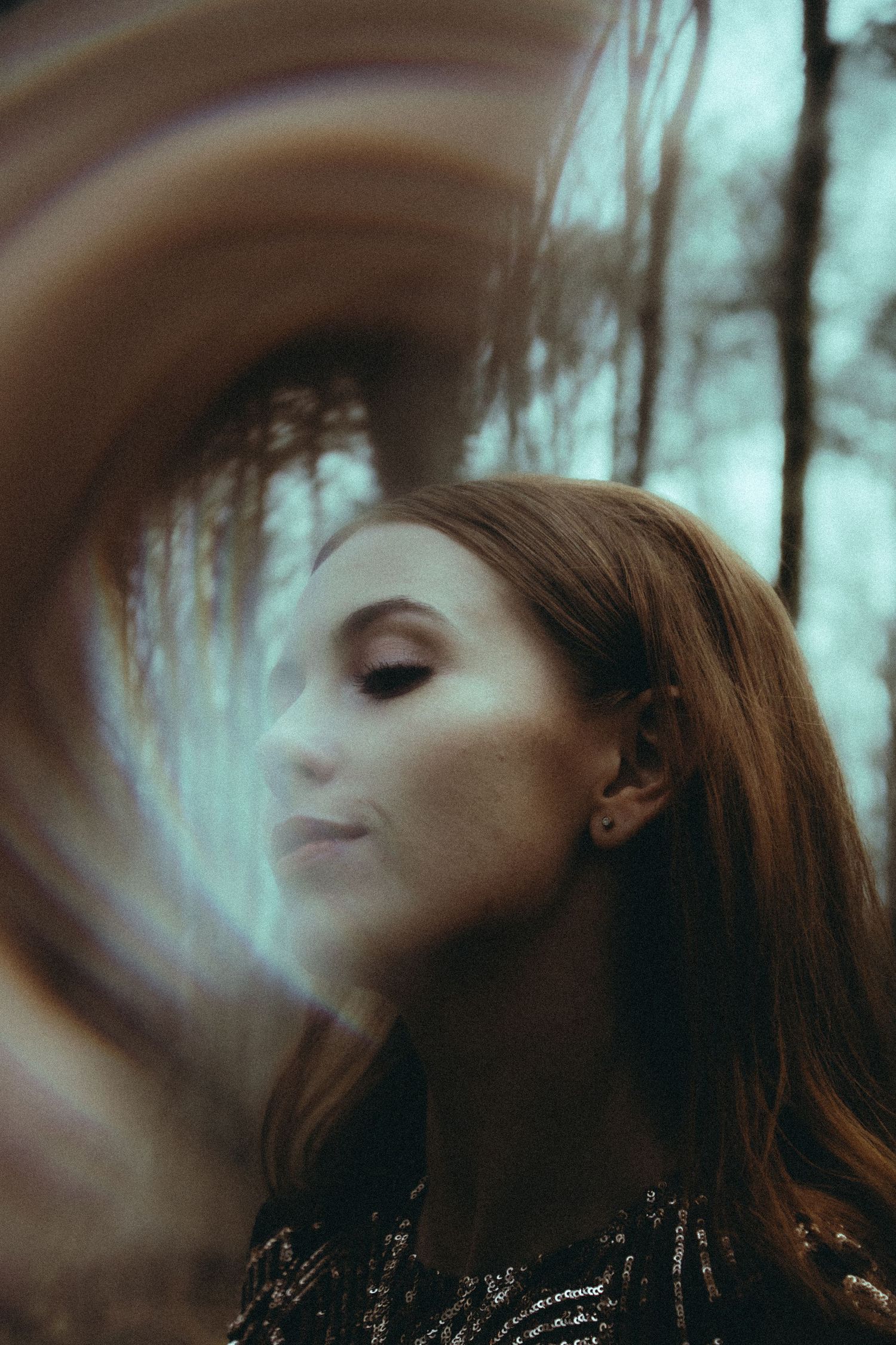 An artistic portrait of a redhead woman with motion blur creating a dreamy swirl effect in a forest setting.