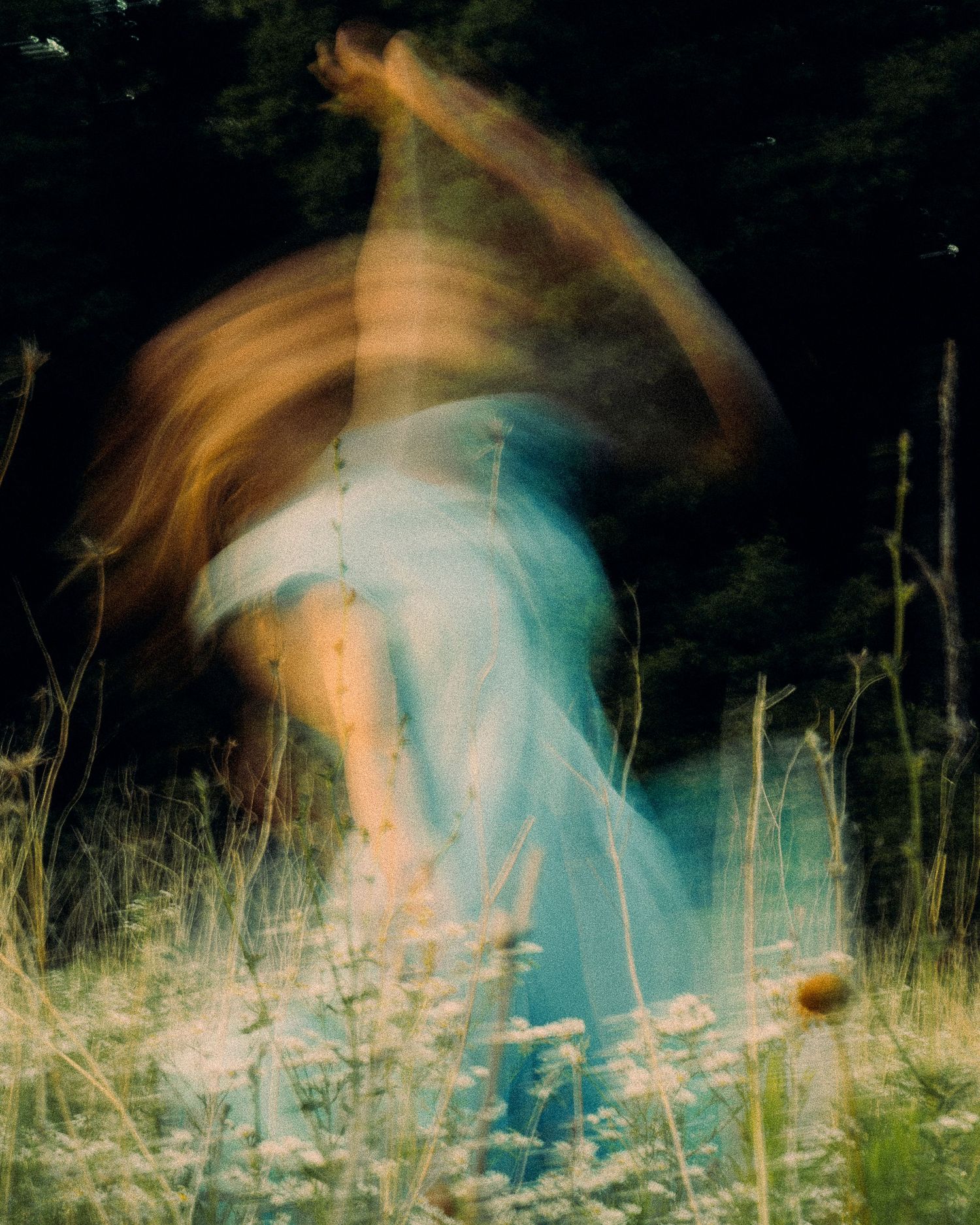 Ethereal motion blur photo of woman in blue dress moving through wildflower field at night.