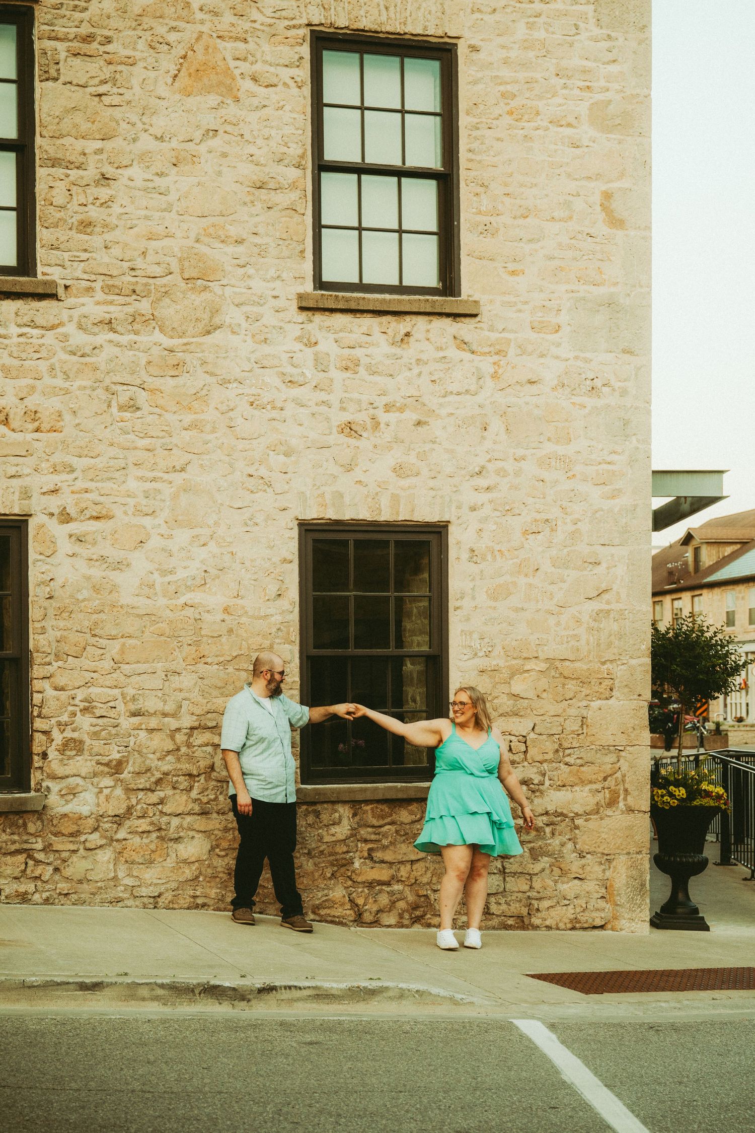 Couple holding hands and dancing in front of a rustic stone building, woman in mint green dress.
