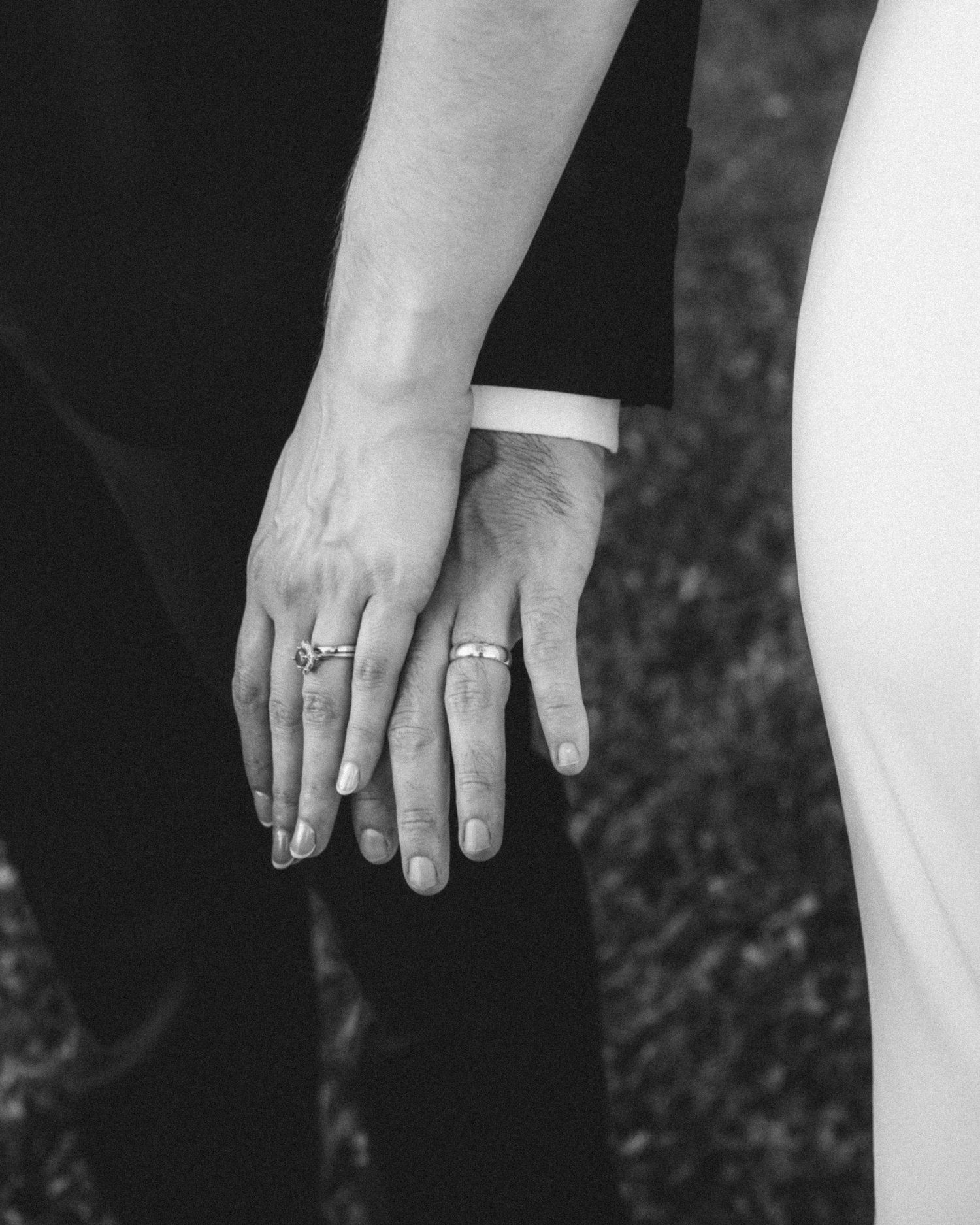 Close-up of newlyweds holding hands showing wedding rings in black and white.