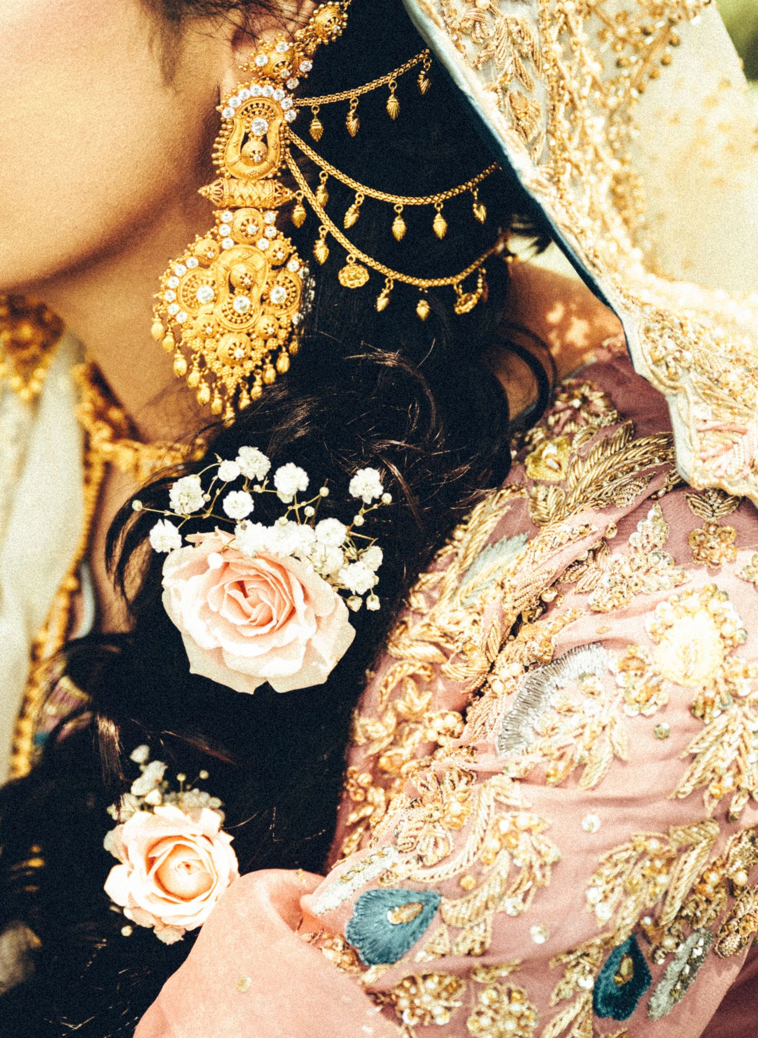 Close-up of South Asian bride showcasing intricate gold maang tikka jewelry and pink roses in her dark hair.