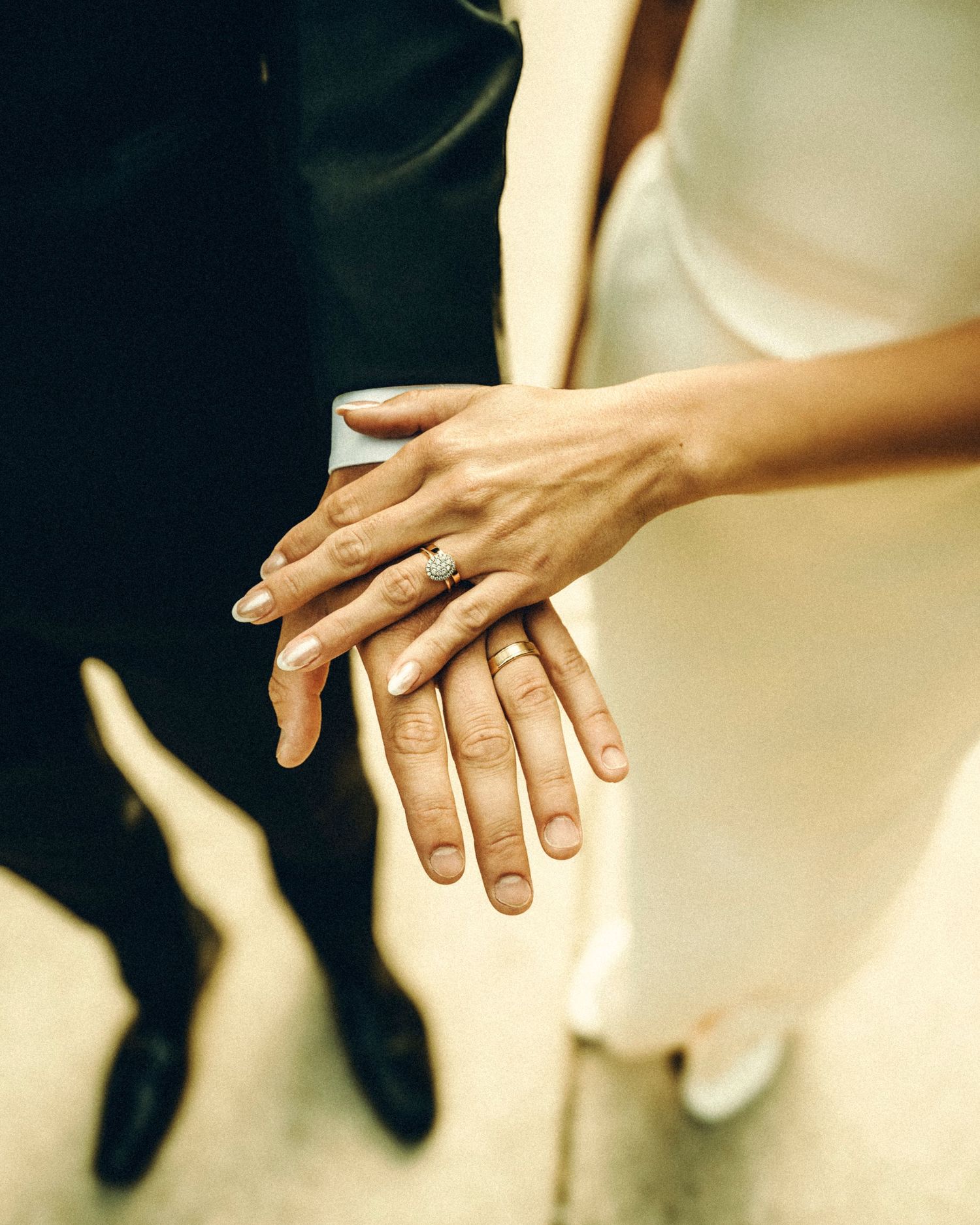 Close-up of newlyweds hands stacked together showing wedding and engagement rings.