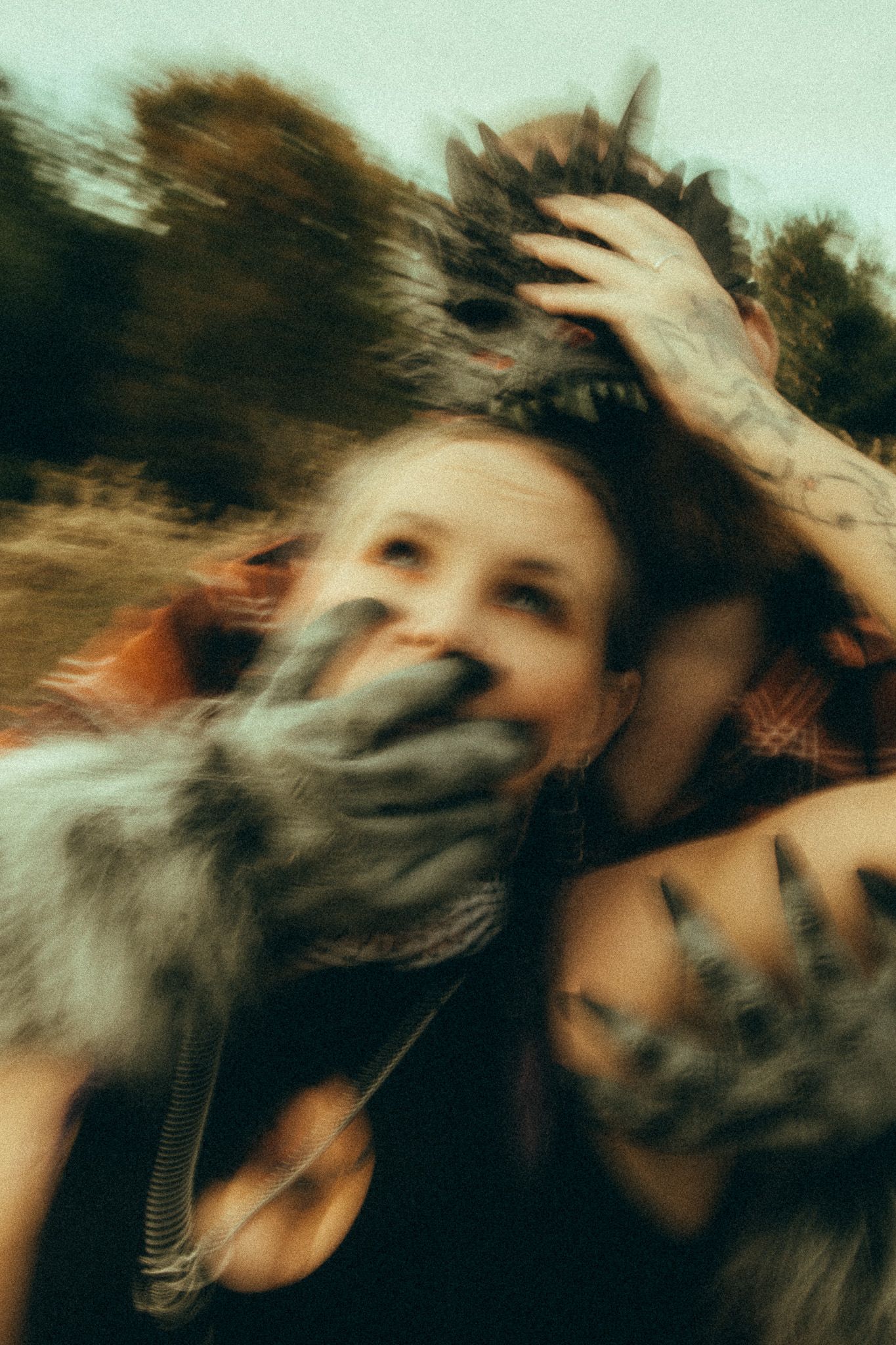 Blurry artistic photo of woman with tattooed hands covering her face outdoors in nature.