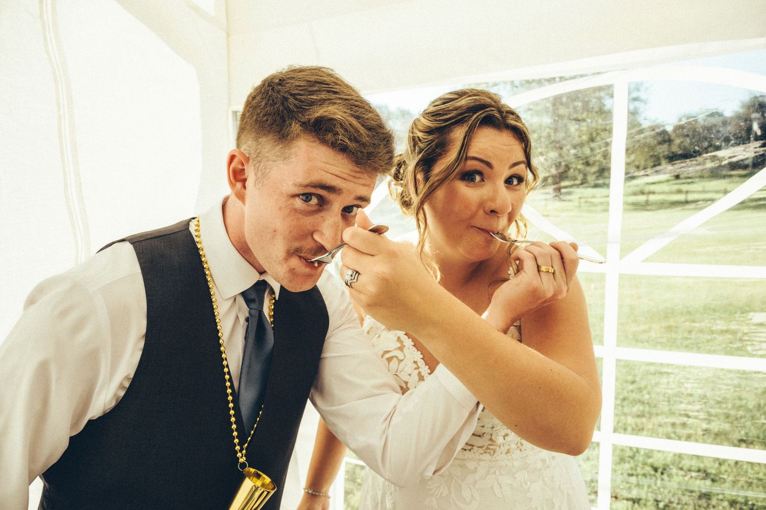 Bride playfully feeds groom a taste of wedding cake inside a bright marquee tent.
