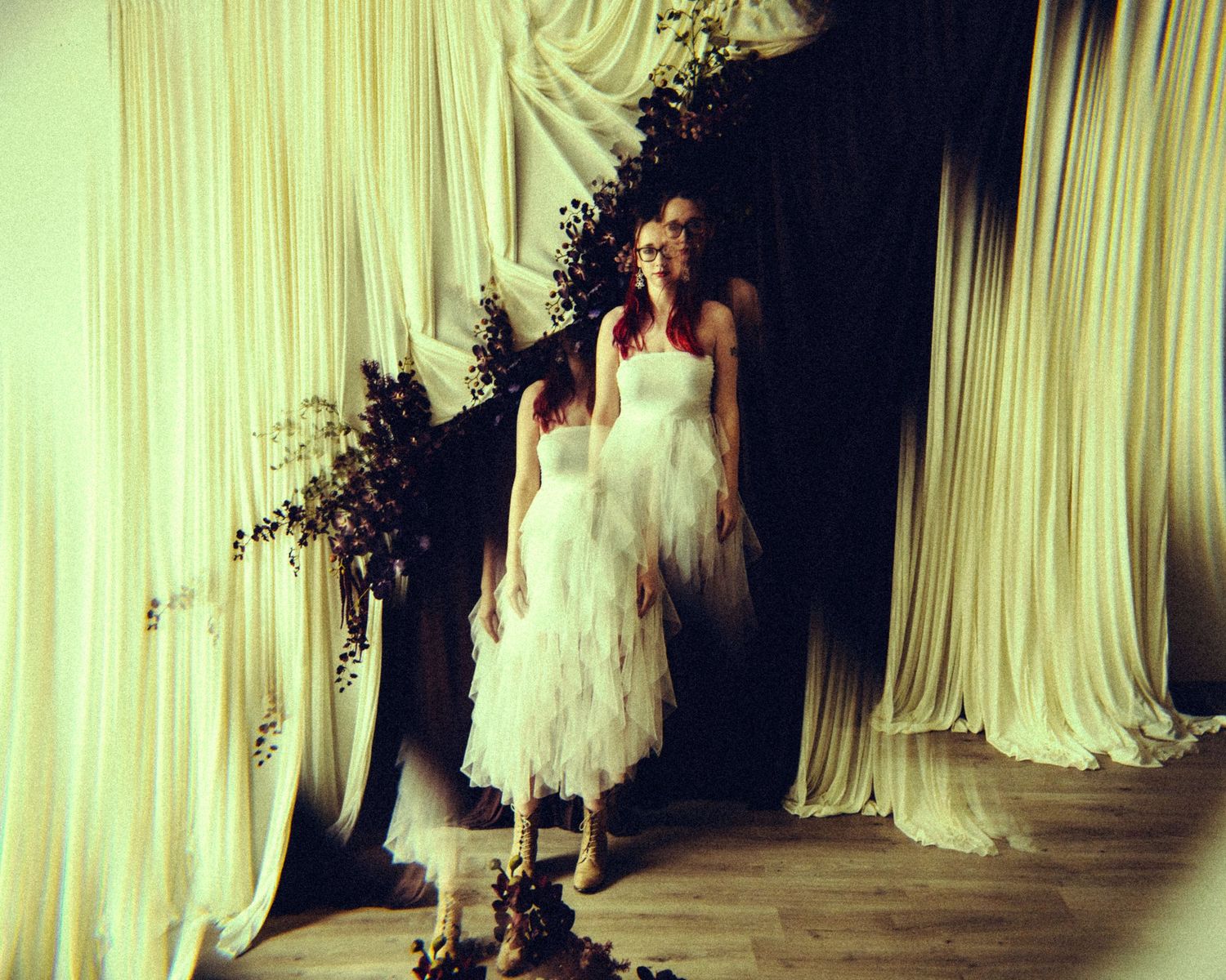 Two women in white tulle dresses standing between draped white fabric curtains indoors.