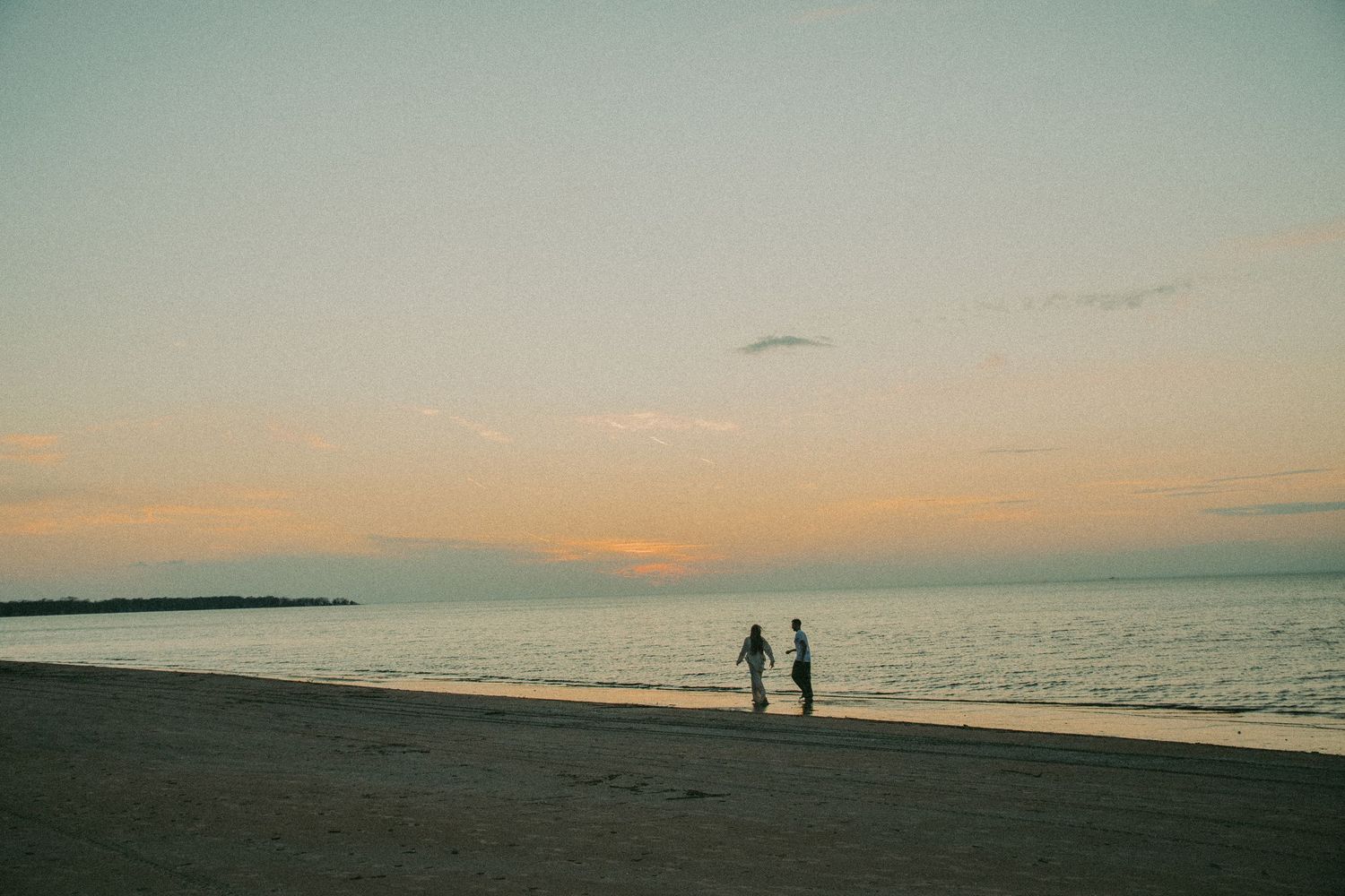 Silhouette of couple walking on beach during pastel sunset by the ocean.