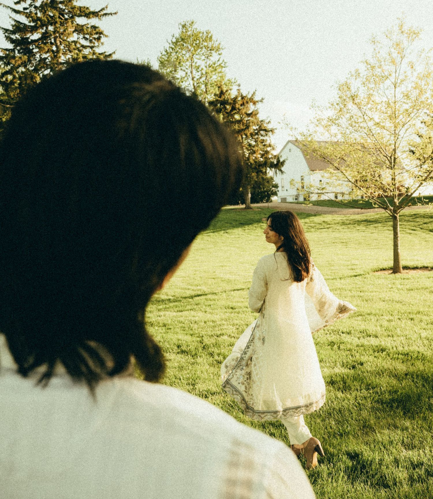 Woman in white dress walking across green lawn during outdoor photo shoot.
