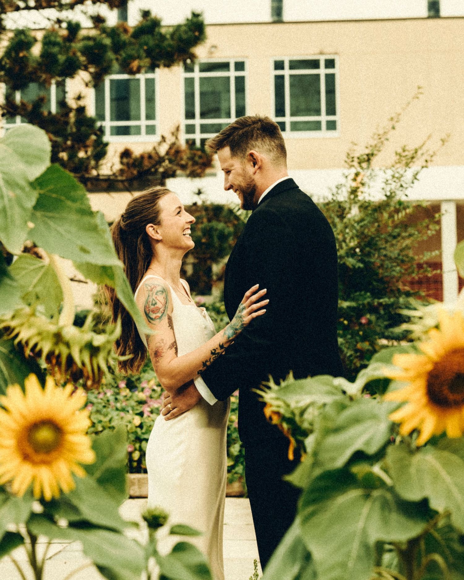 Bride and groom sharing a romantic moment surrounded by sunflowers in a garden wedding setting.